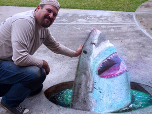 Posing with 3D chalk art of shark in a hole in the ground