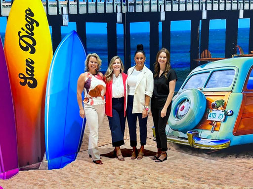 Posing with convention center photo backdrop of San Diego beach, surfboard, woody car, and pier.