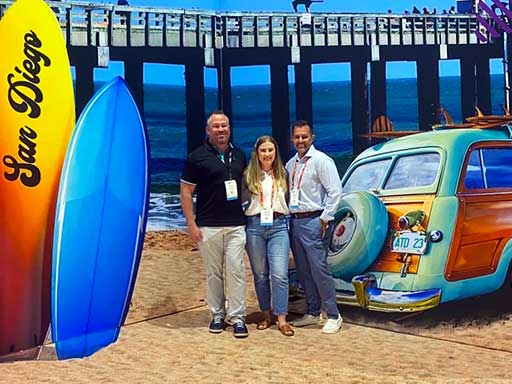 Posing with convention center photo backdrop of San Diego beach, surfboard, woody car, and pier.