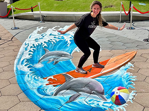 Posing with 3D chalk image of surfboard, dolphins and beach ball.