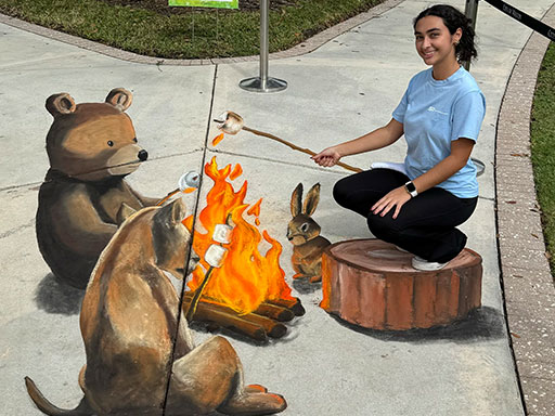 Posing with 3D chalk image of forest animals toasting marshmallows around a fire