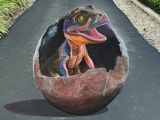 3D chalk art of a baby dinosaur emerging from an egg.