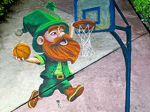 3D chalk art of a St Patricks Day leprechaun playing basketball for March Madness.